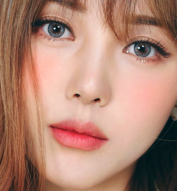 Close-up portrait of a woman with soft makeup, pink lips, rosy cheeks, and light blue eyes, natural lighting and smooth skin texture