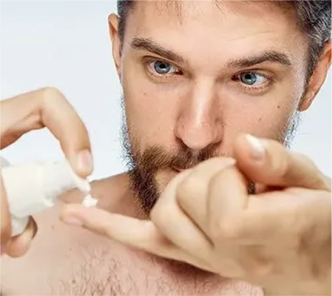 Man applying skincare product to his face using a dropper.