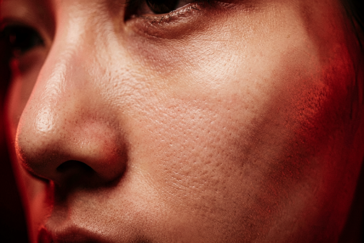 Macro close-up of a woman's cheek and nose with natural skin texture illuminated by deep red light, representing red light therapy for skin at the cellular level, Belldiva