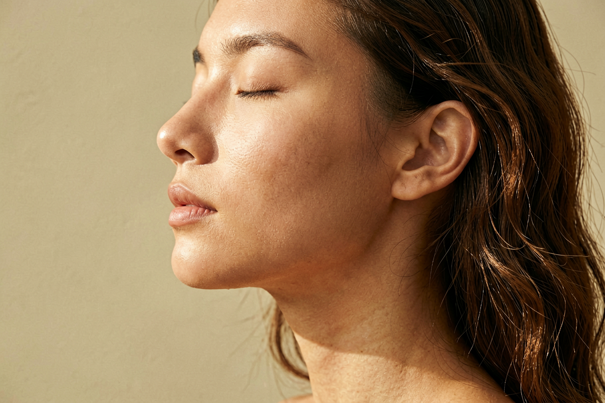 Woman in side profile with eyes closed and luminous even-toned skin bathed in warm golden light, representing the brightening and antioxidant results of a consistent vitamin C serum routine, Belldiva